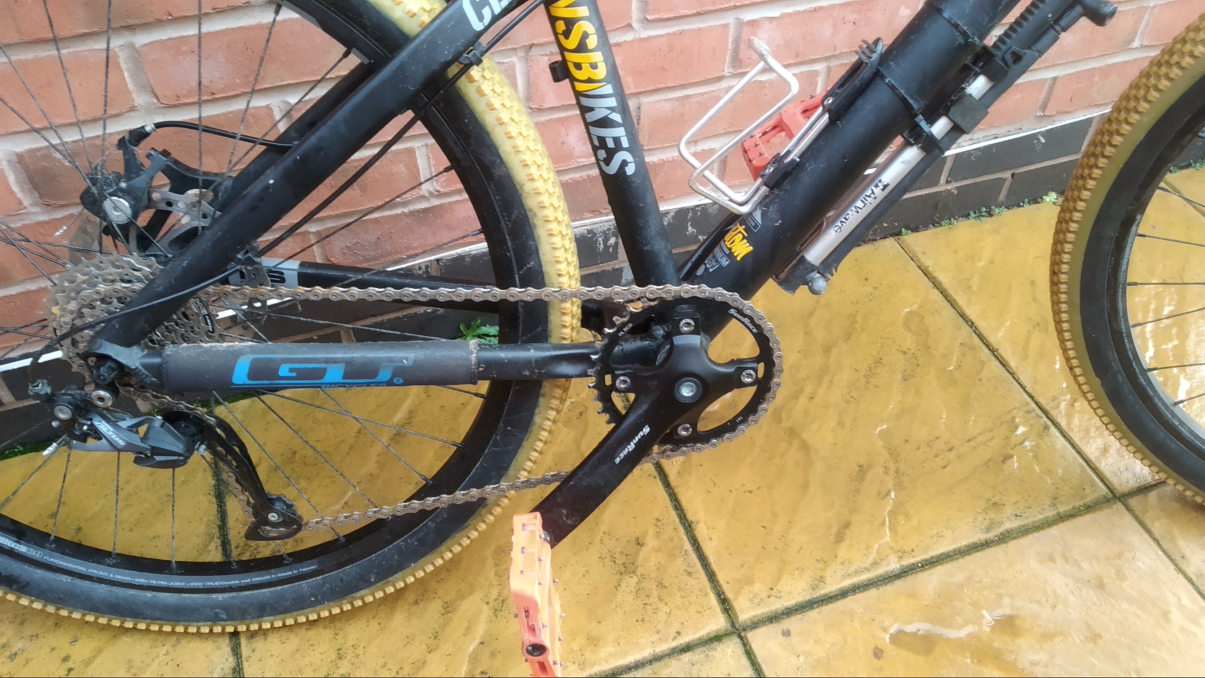 The lower half of a mountain bike. It has yellow tyres, orange pedals, and a basic one by crank