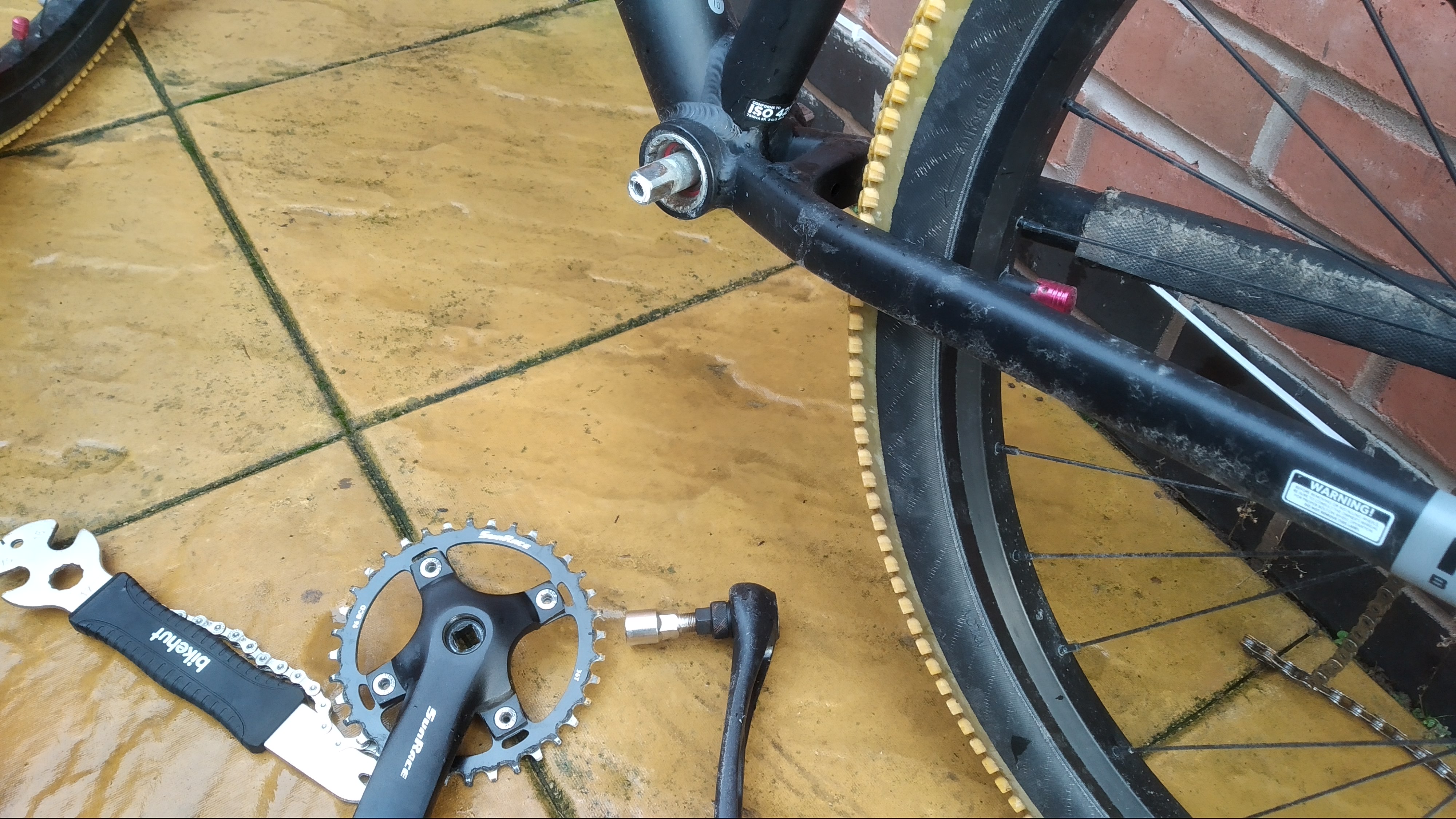 Both cranks on the floor, one with the crank removal tool still in it. A pedal spanner lays next to them. The BB is visible with no cranks on it, still installed in the frame.