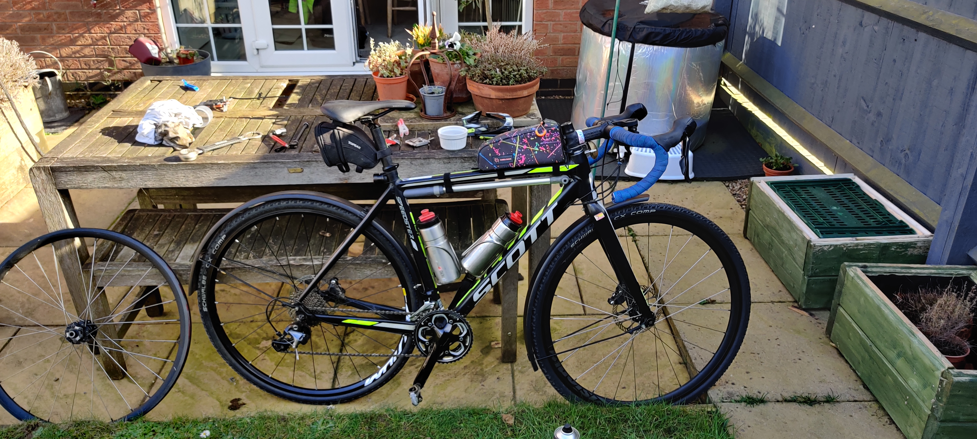 My bike with the back wheel from the above picture still behind it, and the rear wheel that had the cogs on it back on the bike. The front wheel is deeper with the silver spokes and the difference in visual weights between the wheels is visible
