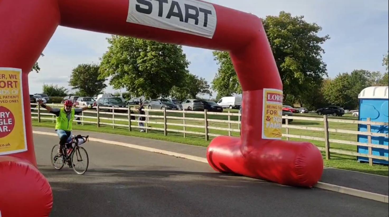 Dad with his arms in the air crossing the finish banner, a large inflatable that says "start" from the photo perspective