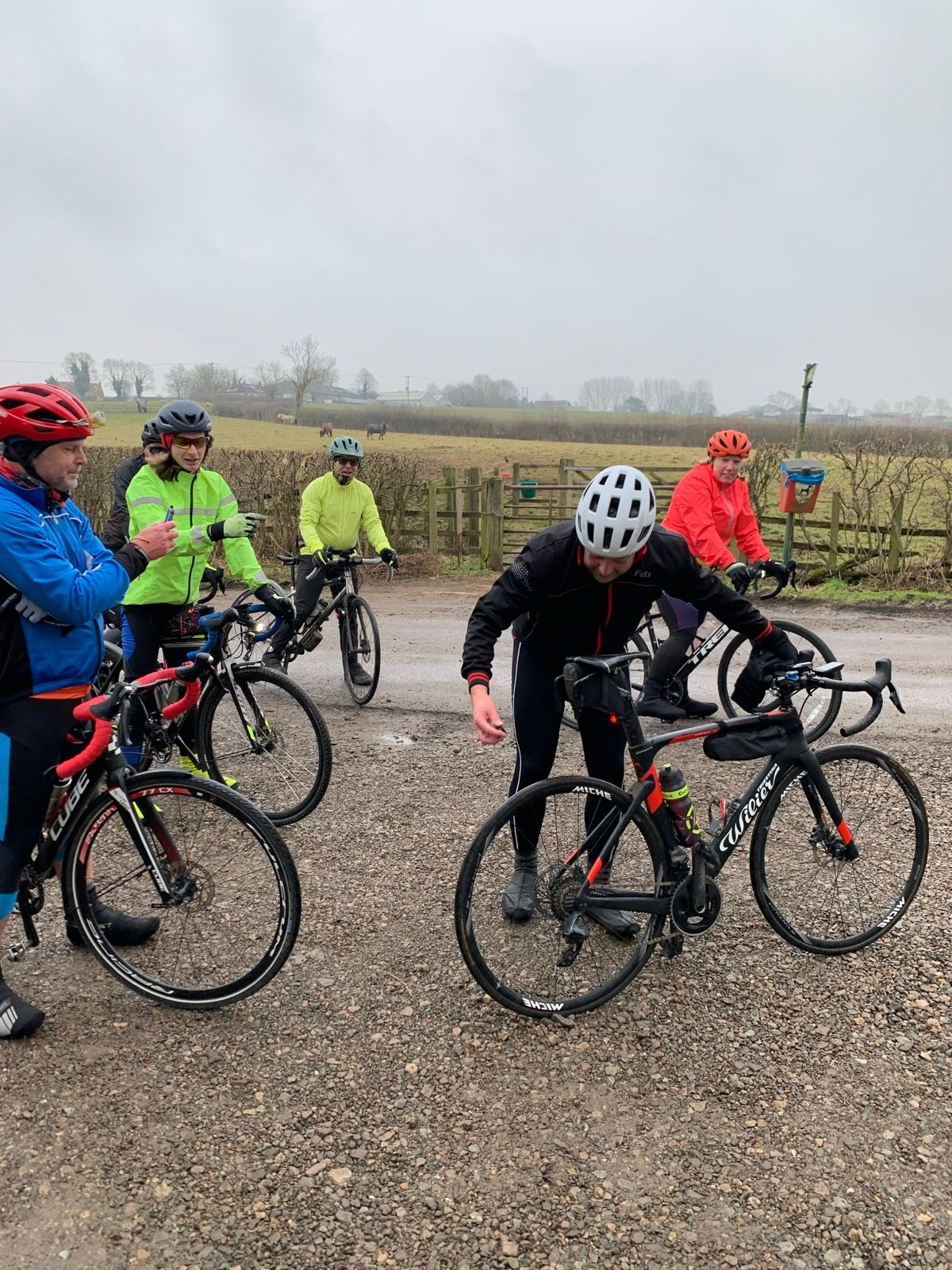 A group of cyclists stood around as one faffs with his bike