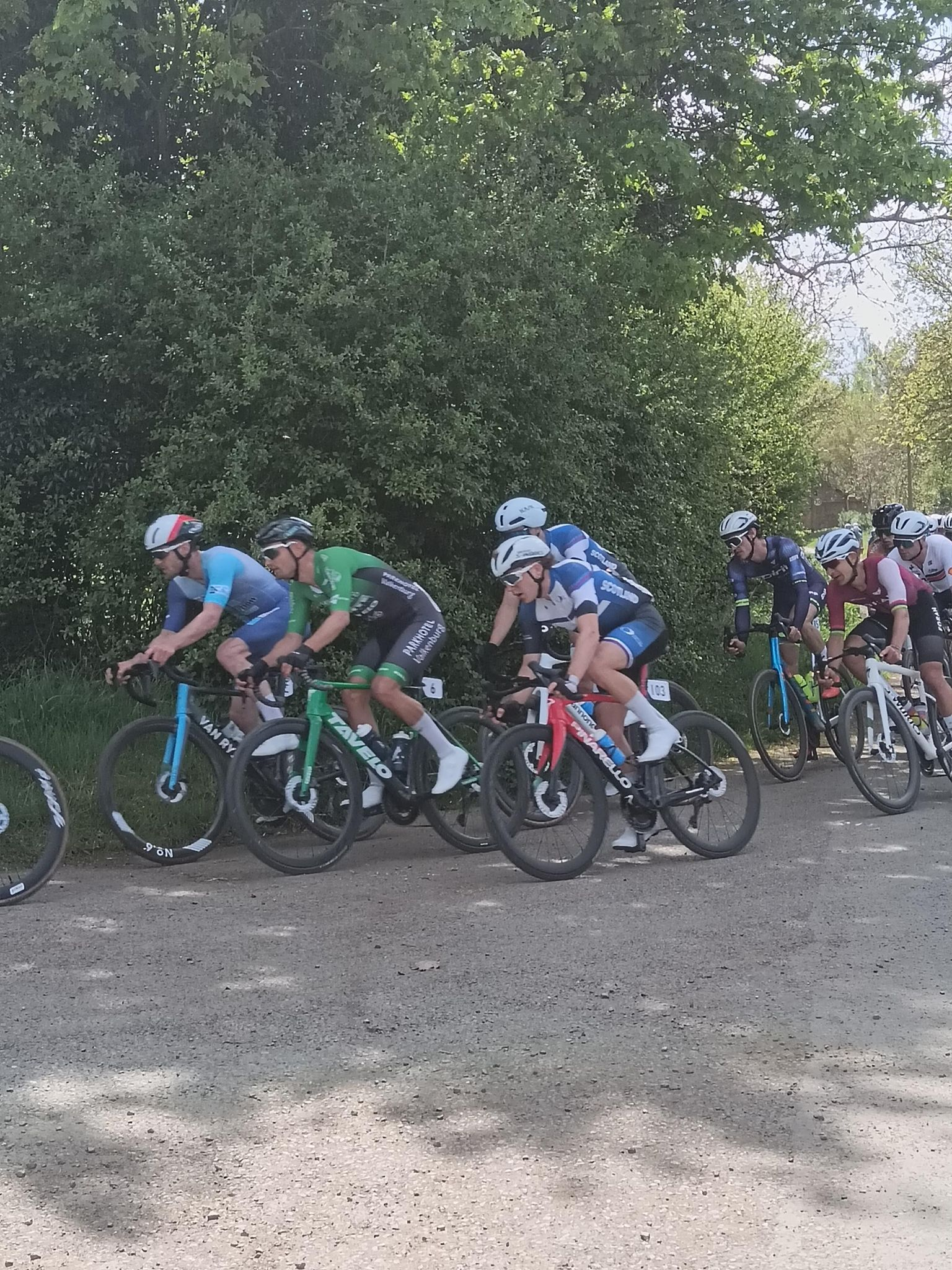 A pack of riders heading from a paved road to a gravel off road, focussed on Team Scotland