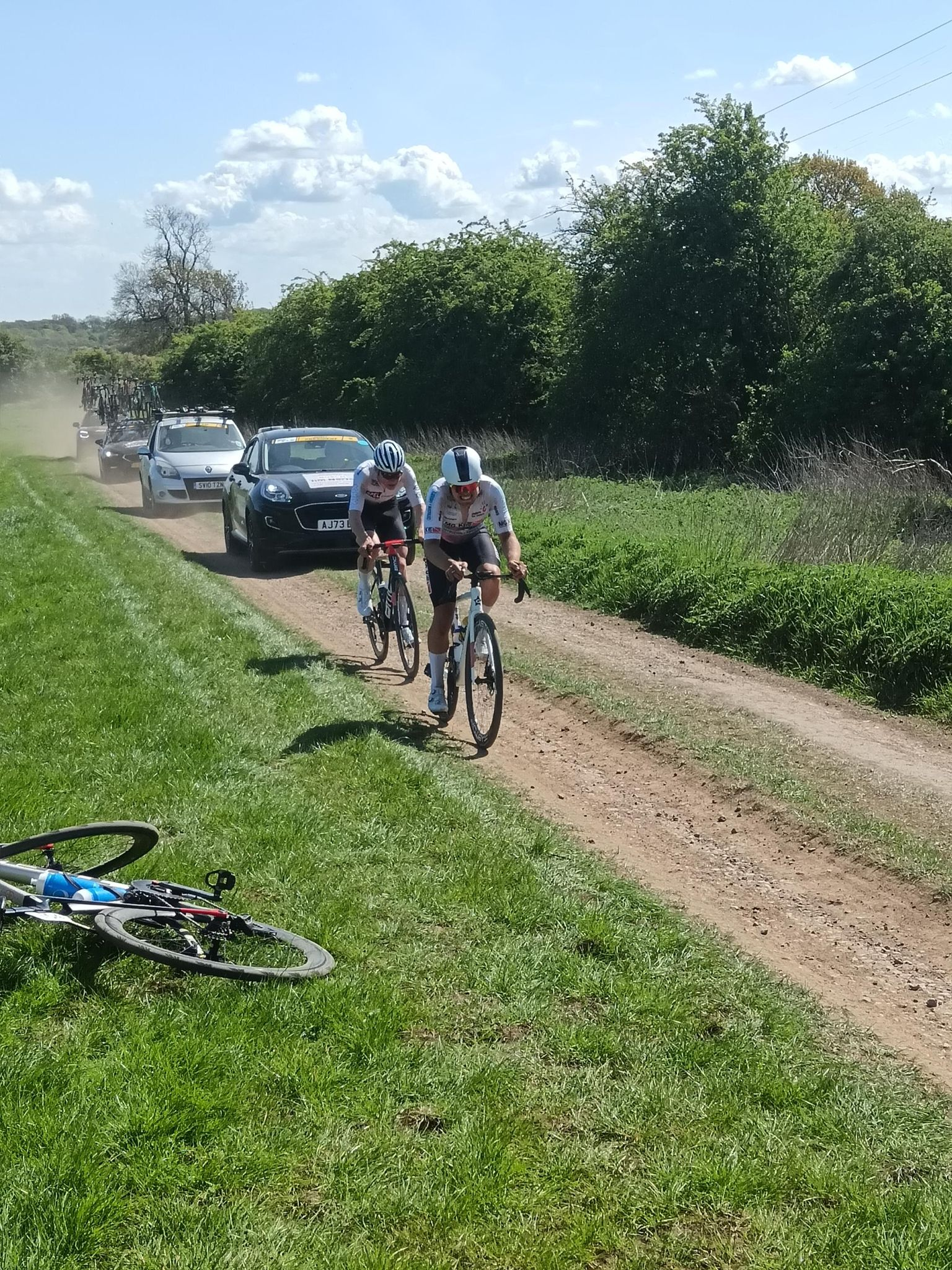 A photo of two riders, and cars kicking up dust behind them