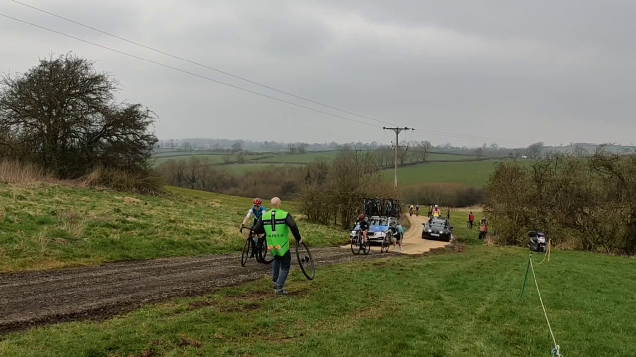 A team member in a bright green vest running to change a puncture for the rider mentioned in the next paragraph. She's running and overtaking riders still on their bikes!