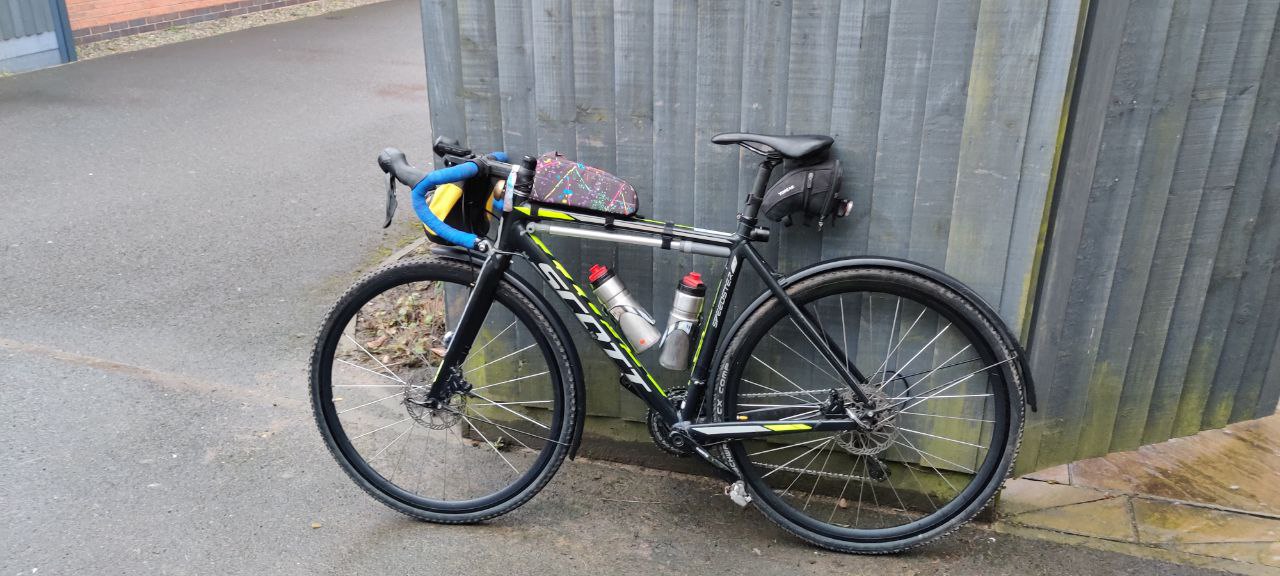 A touring style bike loaded with kit lent against a fense facing out ready to ride