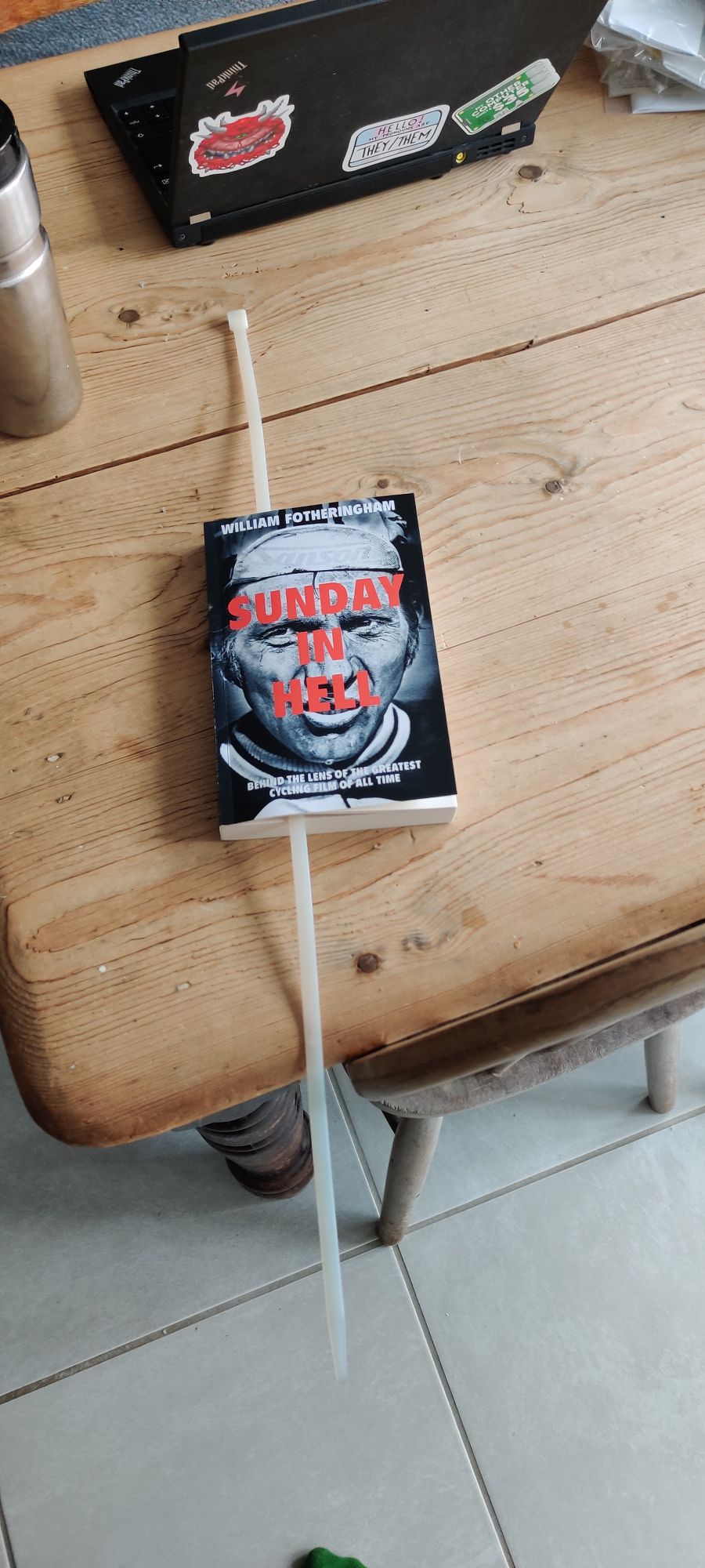 A table with a laptop, waterbottle, and the Sunday in Hell book using a very large 75cm zip tie as the bookmark
